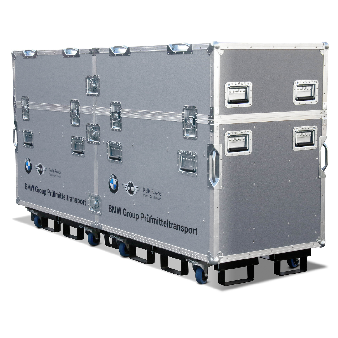 Robustes Transportcase in Silber mit Aluminiumprofilen, zahlreichen versenkten Griffen und Butterfly-Verschlüssen, montiert auf einer rollbaren Plattform; Frontbeschriftung „BMW Group Prüfmitteltransport“ sowie Logos von BMW, MINI und Rolls-Royce.