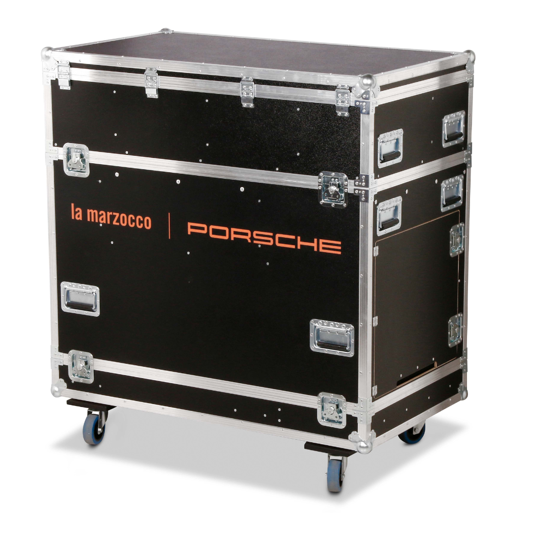 Robustes schwarzes Transportcase mit Aluminiumrahmen, Metallecken und blauen Rollen; auf der Frontseite sind die Markenlogos von La Marzocco und Porsche in orangefarbenem Druck zu sehen.