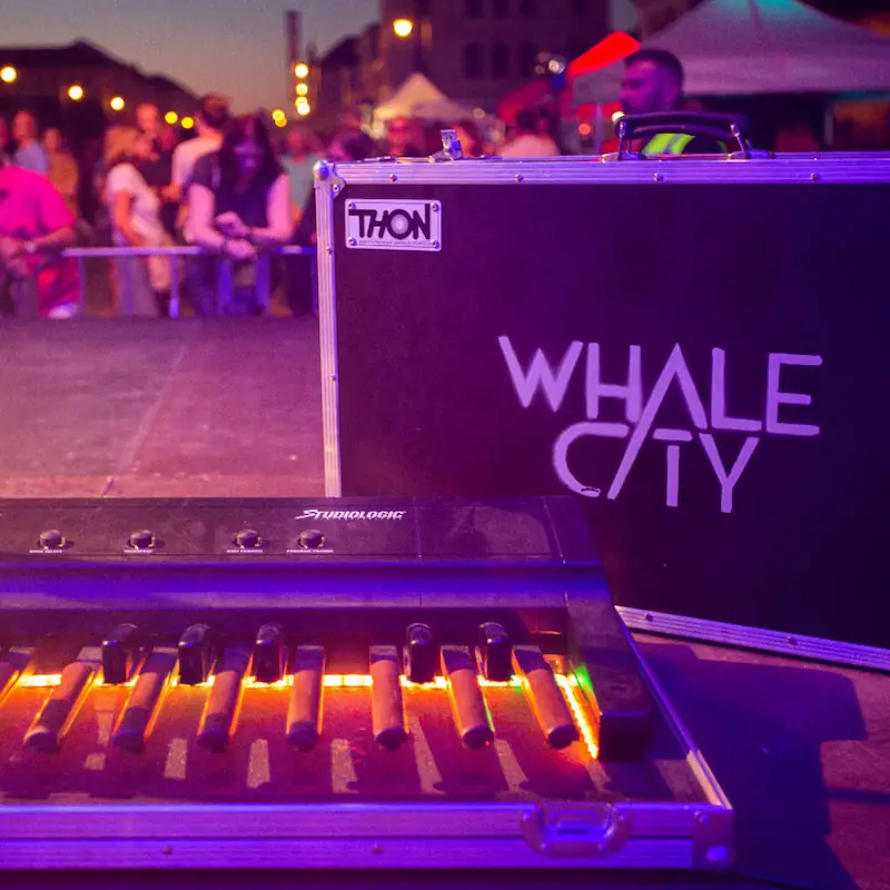 Keyboard-Pedalboard mit Flightcase und dem Schriftzug „Whale City“ auf einer Bühne – Referenzbild eines Kunden.