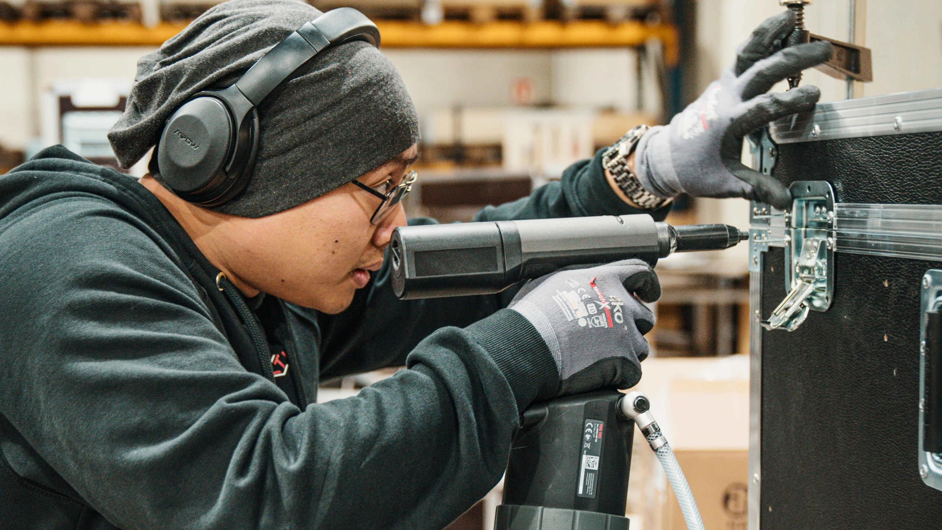 Ein Montage Mitarbeiter von LT-Cases befestigt mit einem Druckluftnietgerät Beschläge an einem Flightcase.