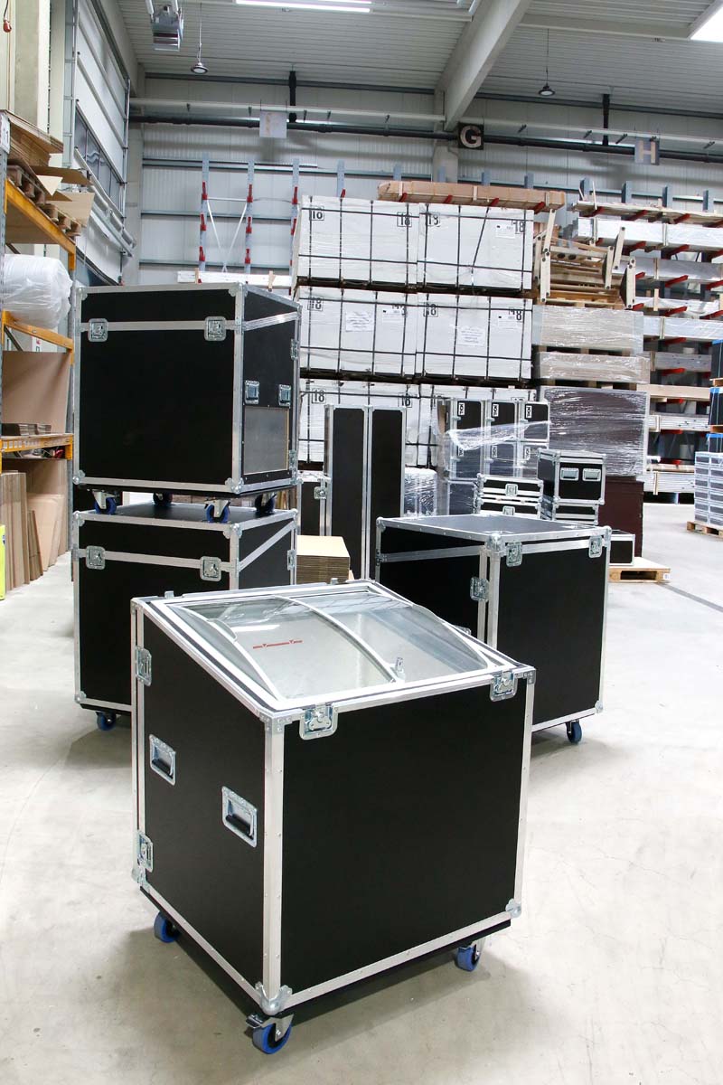 Mehrere stapelbare Flightcases auf Rollen in einem Lagerbereich.
