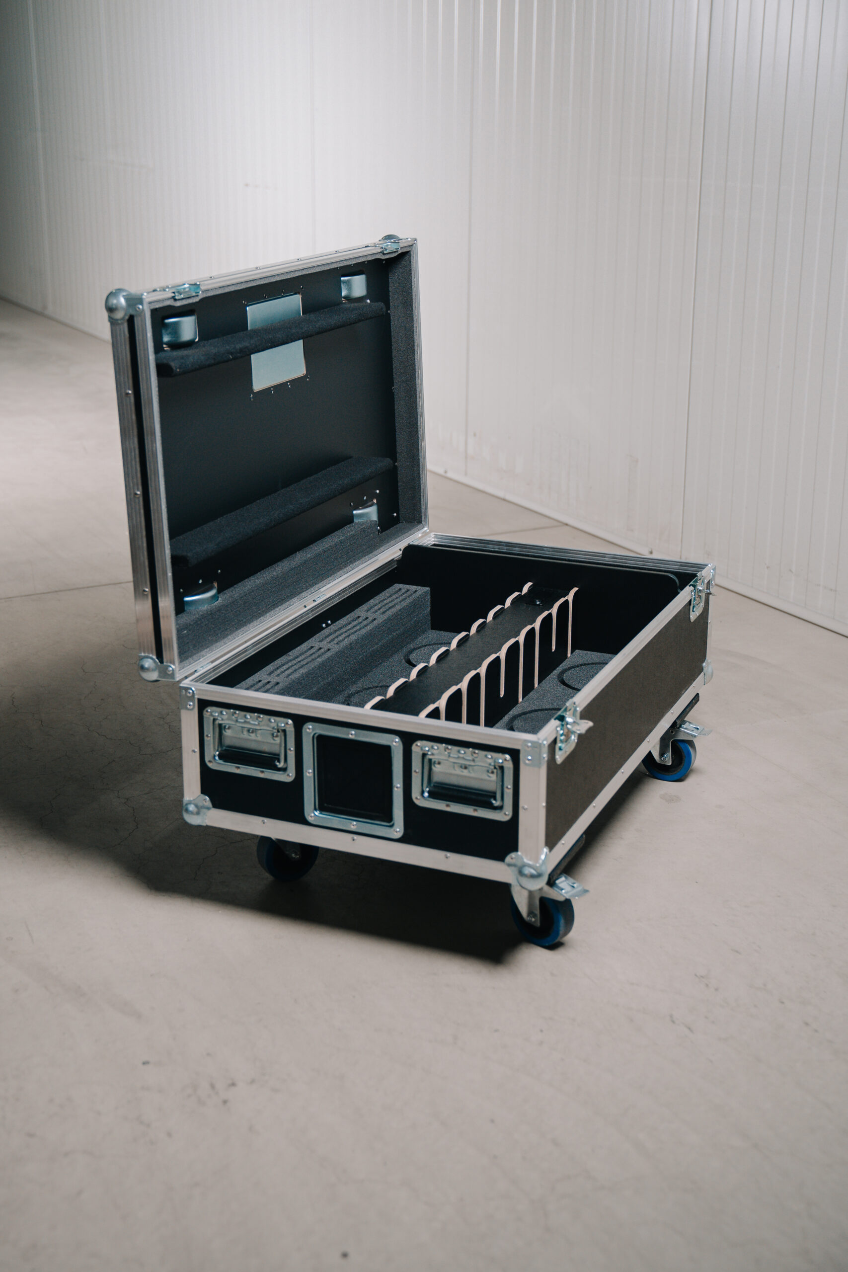 Geöffnetes Flightcase mit gepolsterten Innenfächern und Trennstegen auf einem Werkstattboden.